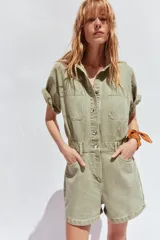 Mono corto de denim azul, con cuello solapa, manga corta, bolsillos delanteros y traseros, cintura elástica en la espalda y cierre frontal con cremallera y botones metálicos.