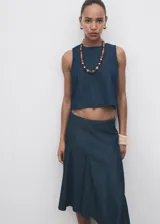Top crop sin mangas, color azul oscuro, con cuello redondo y tirantes anchos. Presenta un efecto denim y cierre de botón en la parte trasera del cuello.