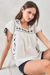 Blusa de algodón color blanco con bordado negro y mangas cortas, detalles de tirantes con borlas.
