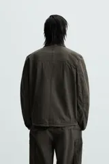 Cazadora color verde oscuro de corte relaxed fit, confeccionada en tejido técnico. Tiene cuello solapa, manga larga con puño abotonado, bolsillos plastrón en el delantero y bajo ajustable con elástico en los laterales. Presenta efecto lavado y cierre frontal con cremallera oculta por solapa con botones a presión.