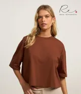 Blusa color beige, cropped y de corte amplio, confeccionada en tejido de media malla, con cuello redondo y mangas cortas.