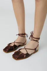 Sandalias bajas de cuero color marrón con tiras finas que se atan al tobillo.