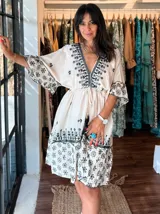 Vestido corto color crudo con bordado floral negro, escote en V, mangas 3/4 acampanadas y cintura ajustable con cordón.