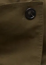 Trench coat color verde militar, de corte recto y largo midi. Presenta cuello de solapa ancha, cierre frontal cruzado con doble botonadura, cinturón desmontable con hebilla y dos bolsillos laterales.