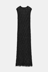 Vestido largo negro, ajustado al cuerpo, con cuello subido y manga sisa. Presenta un tejido con hilo metalizado que le da un acabado brillante.