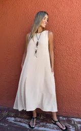 Vestido midi de seda opaca color camel, con silueta en A, cuello redondo y sin mangas. Presenta bolsillos laterales, cortes laterales y un detalle de diseño en la espalda.