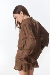 Camisa celeste de lino con cuello clásico, abotonada al frente y mangas largas con detalle de puntilla en los hombros.