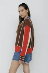 Buzo tipo polo de punto con rayas verticales en tonos beige, marrón y rosa. Tiene cuello polo marrón, cierre parcial con botones amarillos y terminaciones acanaladas en puños y ruedo.