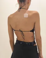 Body negro con estampado floral en lentejuelas grises. Diseño halter con tirantes finos ajustables y aberturas pronunciadas en el torso y los costados.