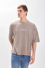 Camiseta manga corta color beige con estampa en la espalda que dice "DON'T STOP UNTIL YOU ARE UNSTOPPABLE", "Let's get lost", "BASED IN SOUTH AMERICA LIVE THE MOMENT Contemporary 1995". Corte amplio y recto, más ancha que larga y sin ajuste al cuerpo.