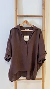 Blusa holgada de lino color marrón oscuro, con cuello camisero y escote en V profundo. Presenta mangas cortas con puños doblados.