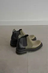 Botines Chelsea de cuero color verde oliva y negro, con elásticos laterales negros, tirador trasero y suela track de goma color verde oliva.