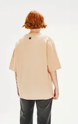 Remera color beige de corte crop y calce oversize, con hombros caídos y cuello redondo.