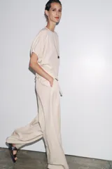 Pantalón palazzo color crudo, confeccionado en tejido fluido con mezcla de lyocell. Presenta tiro medio, cintura elástica ajustable con cordones, bolsillos laterales ocultos en costura y pierna ancha.