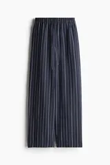 Pantalón de corte holgado en tejido liviano de mezcla de lino a rayas verticales blancas y azul marino. Modelo de tiro alto con cintura elástica y cordón para ajustar fino, bolsillos laterales discretos y piernas rectas.