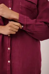 Vestido camisero corto color borgoña de lino italiano, con cuello camisero, manga larga, cierre frontal con botones y dos bolsillos de parche en el pecho con bordado de cerezas.