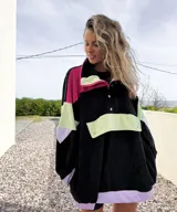 Buzo negro con bloques de color fucsia, verde y lila, con cuello alto con cierre y botones a presión.