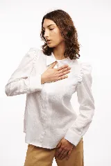 Camisa blanca de lino con corte clásico, cuello camisero, mangas largas con puños abotonados y volados en los hombros.