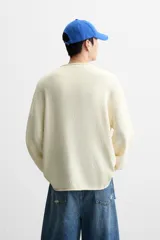 Jersey de hombre color lila, tejido en hilatura de algodón con textura. Tiene cuello redondo, manga larga y acabados en rib con detalle de vuelta.