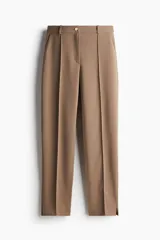 Pantalón de vestir color marrón claro, de tiro alto, con cierre y botón, bolsillos al bies y bolsillos insertados decorativos atrás. Piernas ajustadas con pliegue cosido adelante, raya planchada atrás y tajo corto en los bajos.