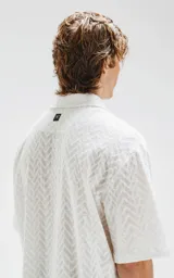 Camisa blanca de manga corta con textura calada y cierre con botones marrones.