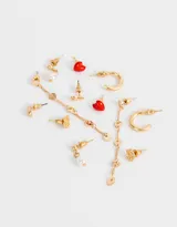 Set de seis pares de aros dorados con distintos diseños: aros tipo botón con forma de flor, aros con forma de corazón rojo, aros con forma de gota, aros tipo argolla y aros colgantes con perlas y corazones.