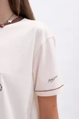 Remera color crudo de manga corta con cuello redondo y ribete marrón. Estampa frontal de Mickey Mouse con texto "Global Explorer Since 1928".