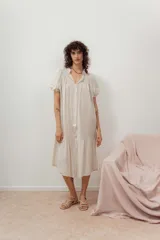 Vestido midi color crudo, con cuello mao, mangas cortas abullonadas, corte recto y falda con volantes.