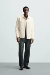 Sobrecamisa negra de tejido con elasticidad, cuello solapa, manga larga con puño abotonado, bolsillos de plastrón en el pecho y cierre frontal con botones a presión.