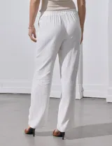 Pantalón de lino a rayas verticales color beige y blanco, con pretina ancha elastizada, lazo de ajuste y bolsillos inclinados.