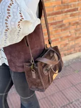Cartera bandolera de cuero color marrón chocolate, con forro de tela y herrajes dorados. Tiene doble asa de mano y correa larga regulable y desmontable. Incluye bolsillo frontal con cierre y bolsillo interno.