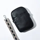 Cartera porta celular negra de cuero sintético con correa de tela estampada con motivos geométricos en blanco, marrón y negro.