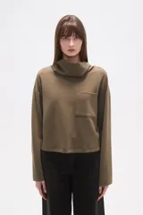 Buzo de manga larga color verde oliva, con cuello tipo tortuga o drapeado y un bolsillo cuadrado aplicado en el pecho. El calce es holgado y el largo es a la cadera.