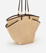Bolso de playa tipo tote bag, confeccionado en paja natural tejida, con asas de cuero sintético marrón y forro interior. Incluye bolsillos laterales y un pequeño bolsillo interno.