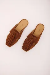 Zueco de cuero gamuzado color marrón, con punta cuadrada y detalle de gran borla de flecos en el empeine. Presenta aberturas laterales y suela plana.