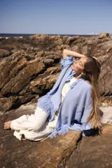 Ruana artesanal de lana merino color celeste claro, con textura tejida y detalles de flecos en los bordes.