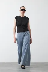 Top sin mangas color beige, confeccionado en tejido acanalado. Presenta hombreras definidas y un recorte fruncido bajo el busto que ajusta la silueta.