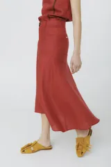 Falda midi color ladrillo, de corte evasé y tiro alto, con bolsillos laterales y botón decorativo en la cintura.