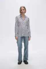 Camisa a rayas verticales grises y blancas, con cuello camisero, cierre frontal con botones, mangas largas con trabillas para enrollar y dos bolsillos de parche en el pecho.