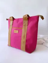 Bolso tipo tote de lona color fucsia con asas de cuero marrón, bolsillo interno y externo.
