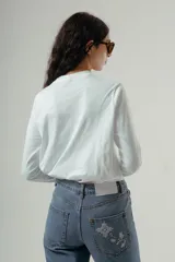 Camiseta de manga larga con cuello redondo, confeccionada en algodón, con un patrón de rayas horizontales blancas y marrones. Presenta un pequeño logo bordado en color rojo en el pecho.