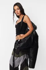 Campera puffer negra de cuerina PU opaca, corte boxy fit, cuello alto con elástico y tancas metálicas, acceso delantero con cierre metálico desmontable y tiracierre de marca, bolsillos ribete con snap metálico y bolsillo superior con cierre metálico cubierto por vista y avío marcario, mangas desmontables por cierre de nylon cubierto con vista, terminaciones de mangas y cintura con elástico interno, forrería al tono, cinta gross estampada nombre de marca y snaps en sus extremos para transportarla al hombro, bolsillo interno de tela base con cierre invisible.