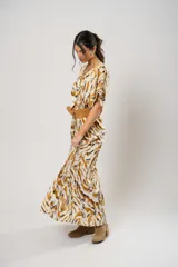 Vestido largo con estampado animal print en tonos camel, blanco y negro. Tiene escote en V, mangas cortas tipo murciélago y tajo frontal. Incluye cinturón ancho de cuero color camel.