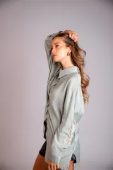 Camisa celeste de corte clásico, con botones frontales y bordados florales en las mangas.