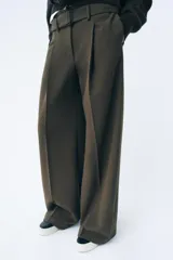 Pantalón de tiro medio color verde oliva, con cintura con trabillas, bolsillos laterales ocultos, cinturón ajustable con hebilla metálica, pinzas delanteras y cierre frontal con cremallera, botón y gancho metálico.