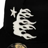 Gorro negro de visera plana con logo de Hellstar bordado en blanco en el frente. El diseño incluye una estrella, un rostro y llamas.