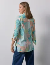 Camisa estampada con hojas en tonos celeste, naranja y verde. Tiene cuello con solapa, abertura central con botones, bolsillos aplicados en la parte delantera y mangas 3/4 con lazo.