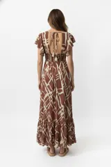 Vestido largo estampado en tonos marrón y beige, con mangas cortas tipo mariposa, escote profundo con lazo ajustable en el centro del busto y falda con volados en el ruedo.