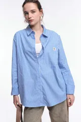 Camisa celeste a rayas verticales blancas, de corte holgado, manga larga y cuello camisero.