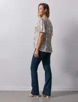 Blusa de tejido elastizado con estampado geométrico en tonos beige y blanco. Tiene cuello redondo con escote en V y lazo de ajuste, y mangas cortas amplias. Marca Cupio.